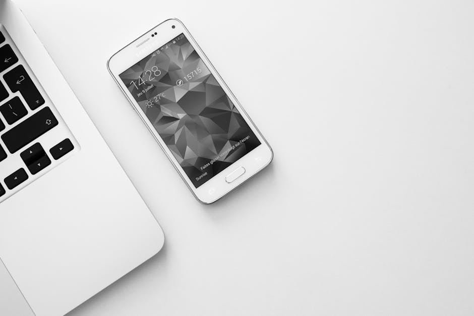 A minimalist office desk with a laptop and smartphone displaying a geometric wallpaper.